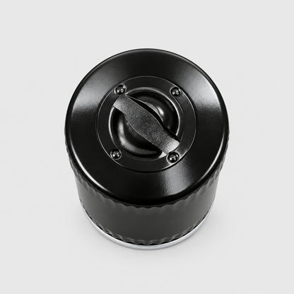 A close-up top-down view of a black plastic bottle cap or container lid placed on a light wood-grained tabletop.